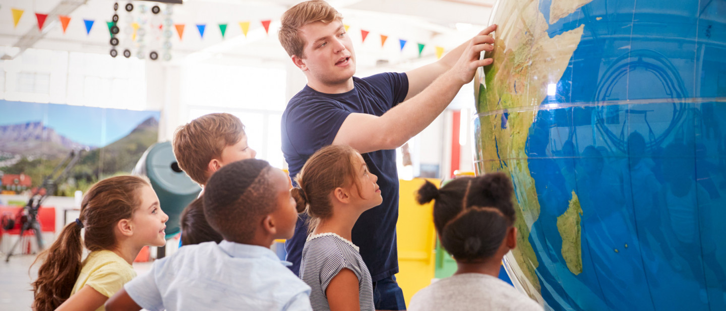 Teacher showing grade schoolers where a location is on a world globe. 