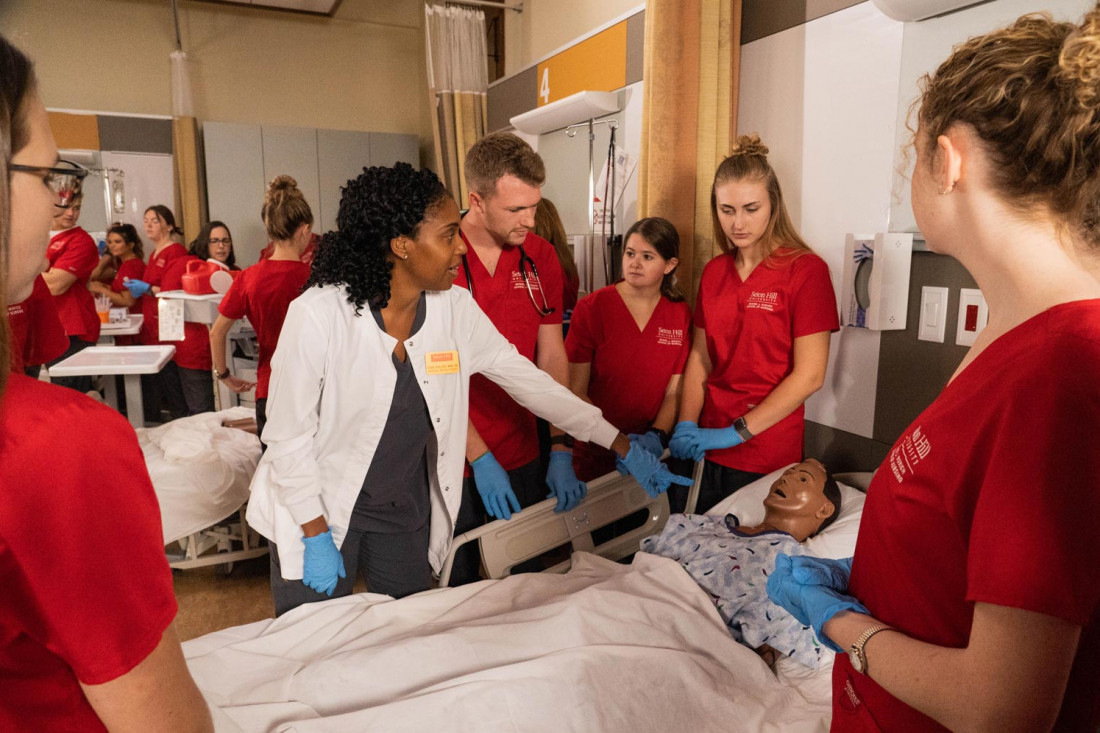 Nursing students learn from their professor in a lab. 